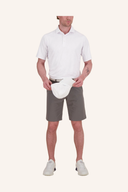 Männliches Modell trägt weißes Poloshirt mit kurzen Ärmeln, graue Shorts und weißen Gürtel, kombiniert mit weißen Golfschuhen vor neutralem Studiohintergrund