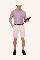 Männliches Modell trägt ein mauve-farbenes Kurzarm-Hemd mit feinem Muster, rosa Shorts, schwarzen Gürtel und schwarze Wanderschuhe. Das Modell hält eine schwarze Flasche in der Hand und steht vor neutralem cremefarbenem Hintergrund.
