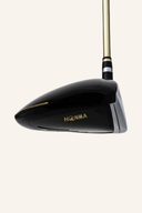 Honma Beres 09 3-Sterne Driver, Golfschläger mit schwarzem Griff und goldener Kopfpartie, auf einem Golfplatz liegend